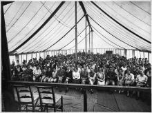 Large group seated inside a tent.