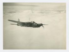 Black and white photograph of a plane flying in the sky.