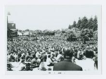 Large group of people outdoors, sitting on the ground. 