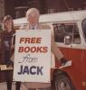 Jack McClelland standing outside holding books while wearing a "Free Books from Jack" sign 